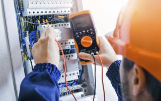 Das Foto zeigt einen Elektroinstallateur, der die Elektroanlage in einem Verteiler prüft.