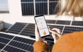 Das Foto zeigt eine Frau, die mit einem Smartphone in der Hand auf einem Dach voller Solarpanele steht.