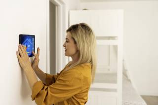 Bild einer Frau, die auf einem Smart Home Display die Raumtemperatur reguliert